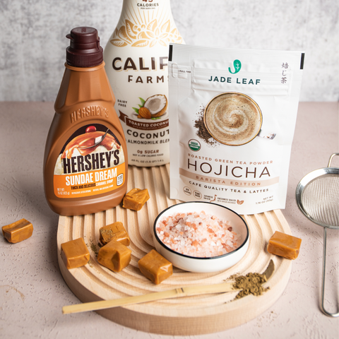 Image of bottles of caramel syrup, almond milk, Jade Leaf Hojicha Powder on a table