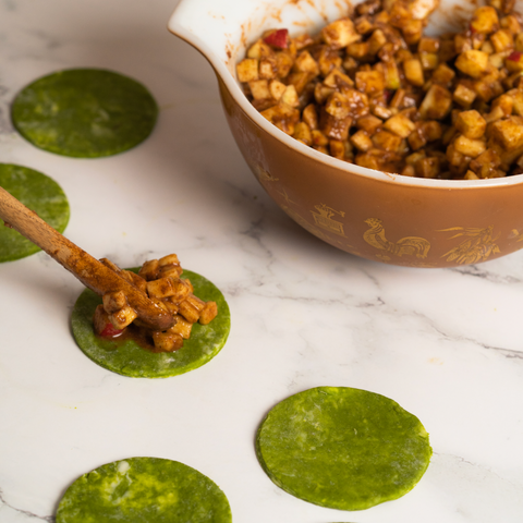 Wooden spoon scooping apple mixture into mini matcha pie crusts