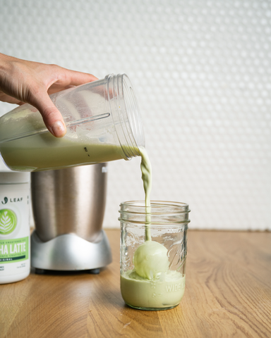 Barista pouring a blended foamy matcha latte on ice.