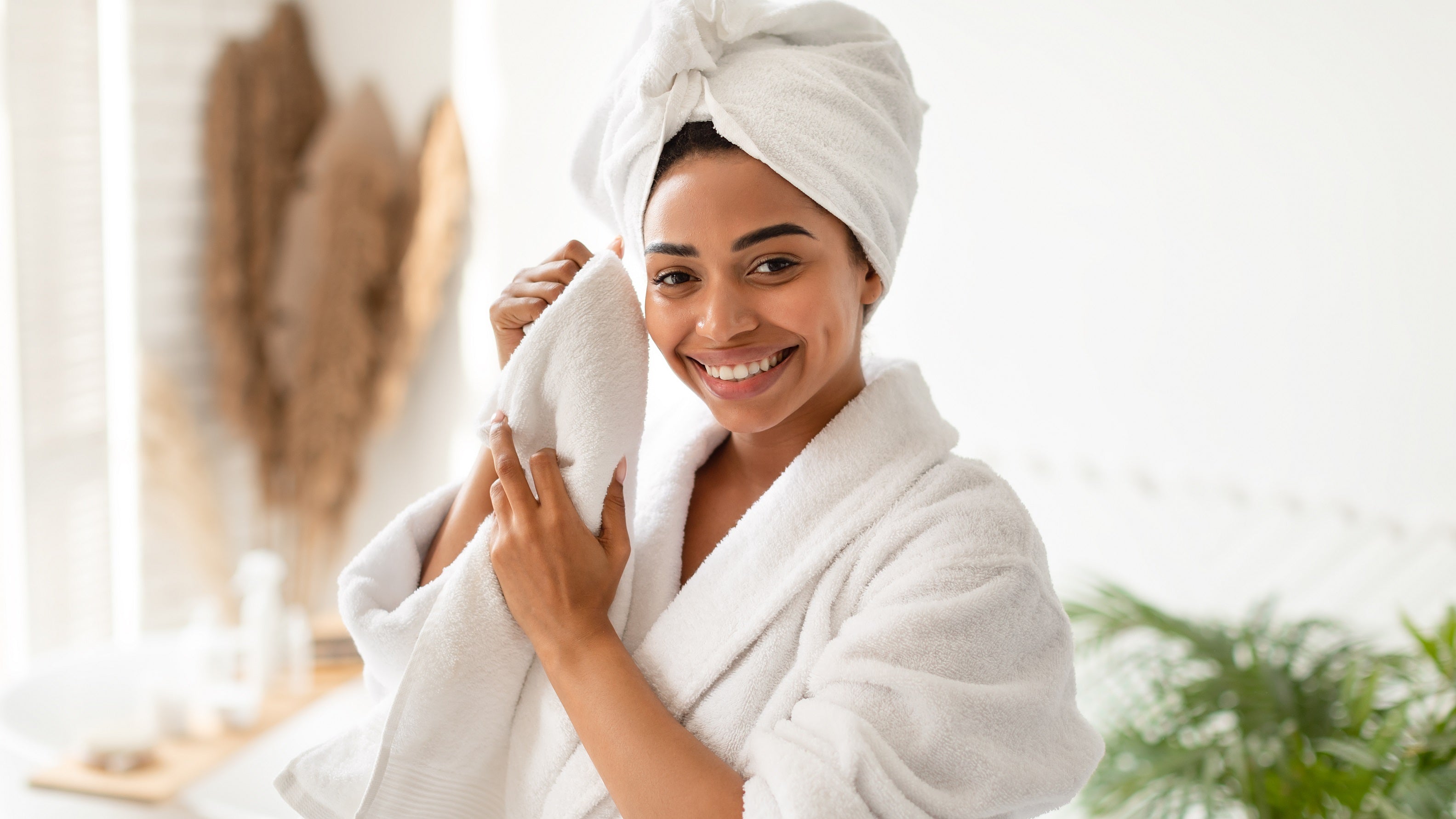 Black woman in robe and hair towel smiling after cleansing skin with KAIKE Melt Oil Cleanser