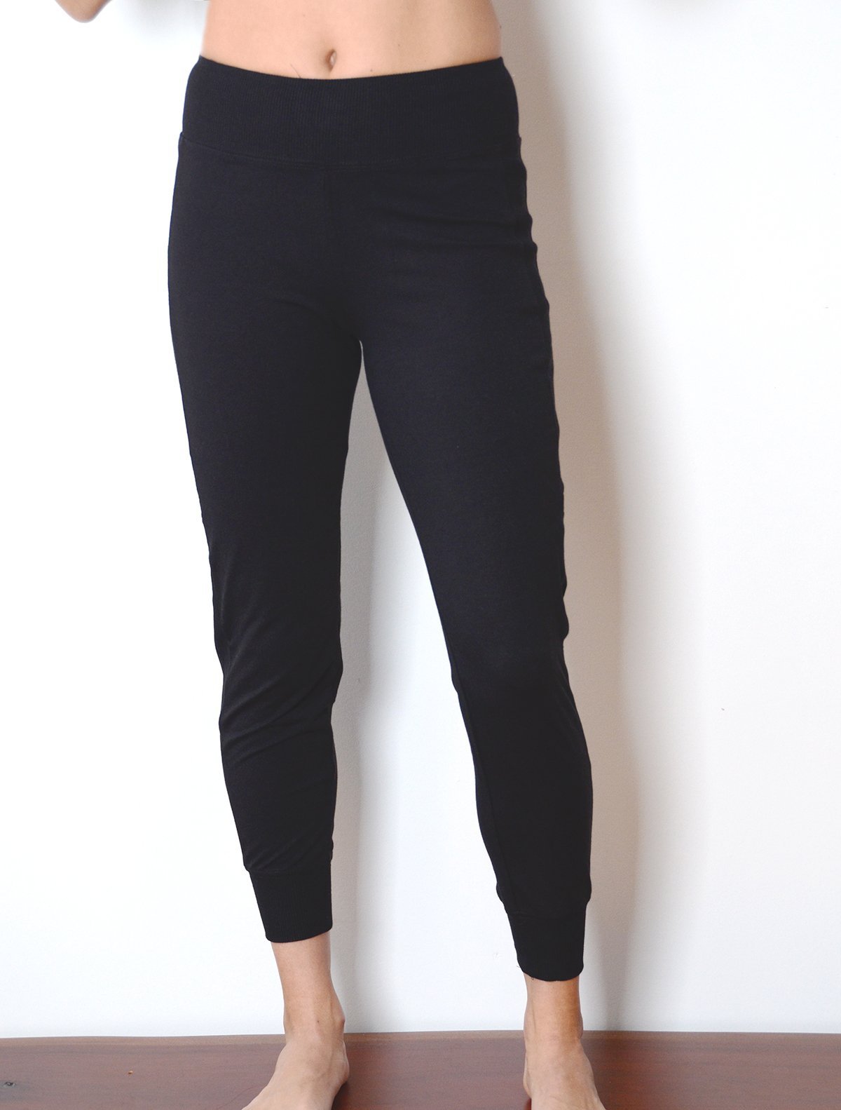 front view of model wearing simulacra's women's black cropped joggers with bare stomach to show the high rise shape