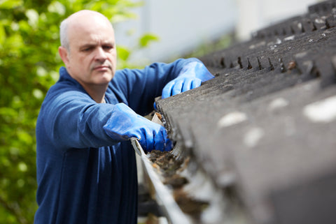 man cleaning out leaves from gutter for fall