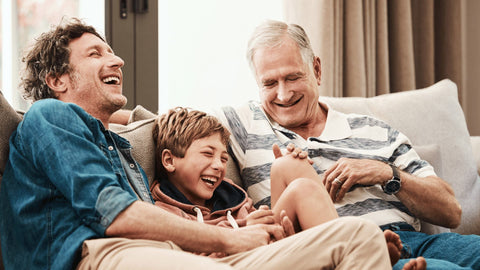 an elderly man, and adult man, and a male child sitting on the couch laughing