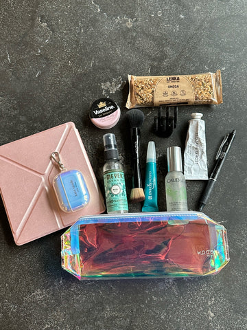 Spread of objects in Andreas bag contains Airpods pro, Kate Spade's AirPods Pro Case, a Kindle, Kindle Pink case, Lenka bar, Hair clips, the prism pouch, the secret brush, erasable pens, byredo hand cream, cuticle rehab, and the Caudalie Beauty Elixer