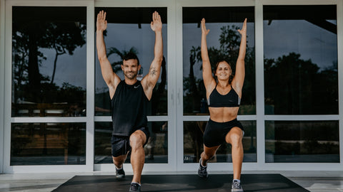 man and woman raising hands while exercising on large exercise mat