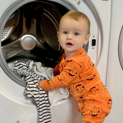 Little boy in Halloween pajamas loading a washer