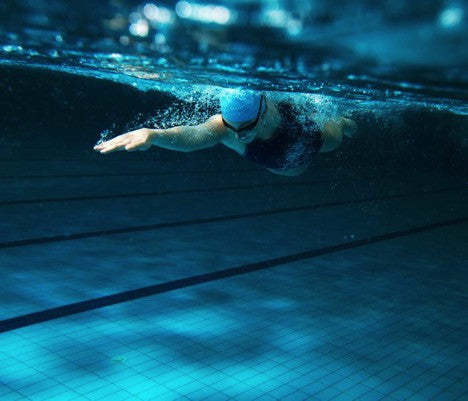 A female swimmer reaches underneath the surface of the water during the freestyle swim stroke. 