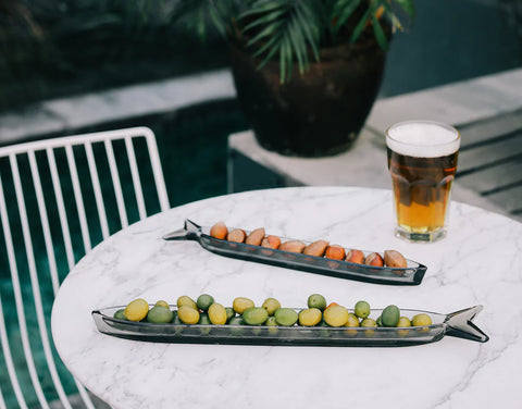 deux assiette apéritifs en forme de poisson avec des olives vertes et  brunes posé sur une table à la nappe blanche