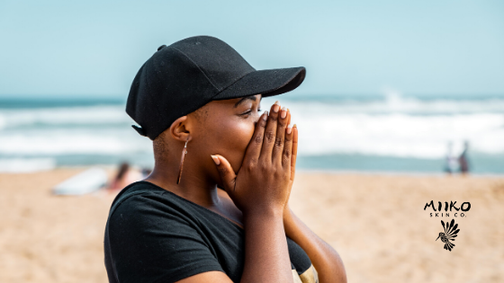 girl with black hat at the beach holden hands to face