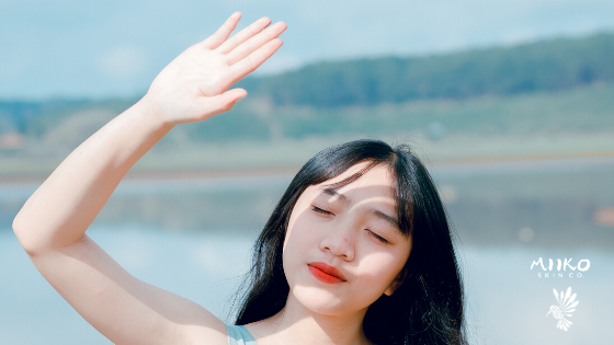 asian girl with red lipstick holding hand up to the sun with closed eyes