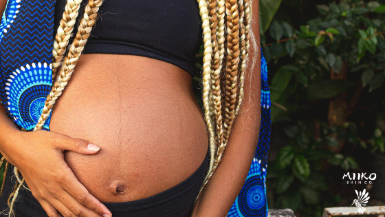 Pregnant human is holding their belly, while wearing a sports bra to show off the belly to the camera