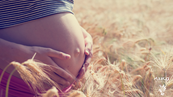 Pregnant person holding their belly standing in a field of grasses