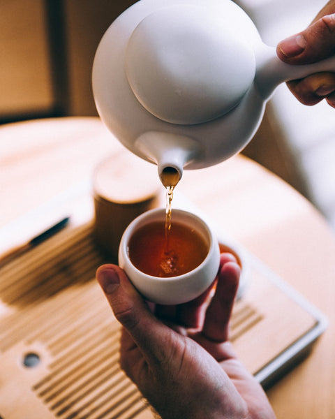 Close up image of herbal tea being poured into a small tea cup. 