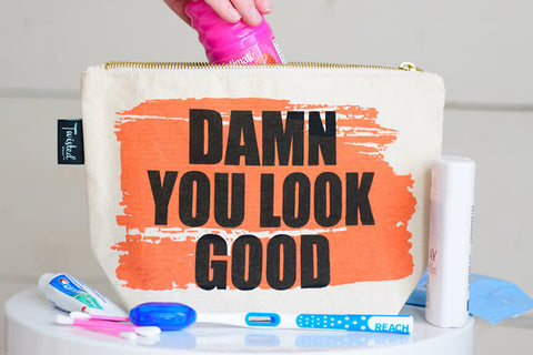 Cotton canvas, zip pouch with gold zipper, screen printed design with bold text that reads "Damn You Look Good"