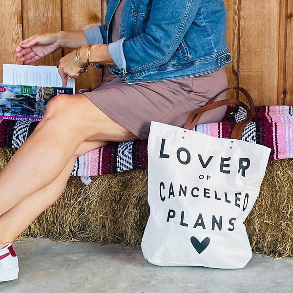Lover of Cancelled Plans tote bag next to model sitting on hay bale reading a magazine