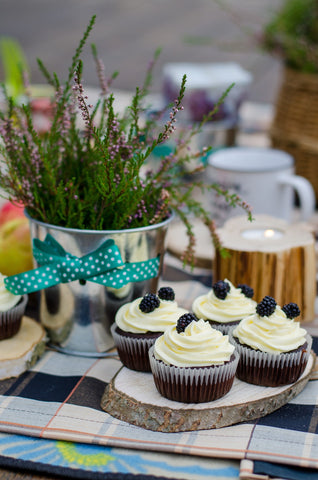 picnic set up with cupcakes on a wood slice and beside a rustic vase of herbs sitting a blank