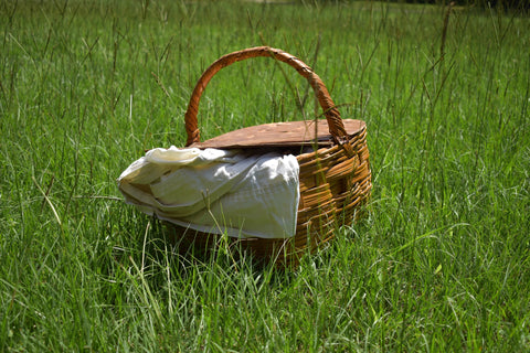 wicker picnic basket with a white blanket hanging out of it sitting in the grass