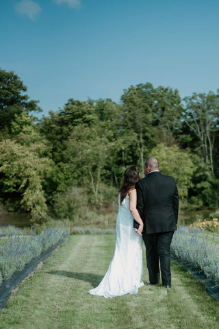 bride and groom standing in lavender field looking over a pond with trees in the background