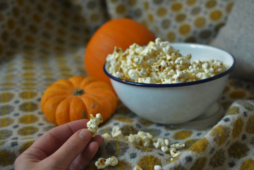 hand taking popcorn from a bowl on top of a yellow spotted wool blanket and pumpkins in the background