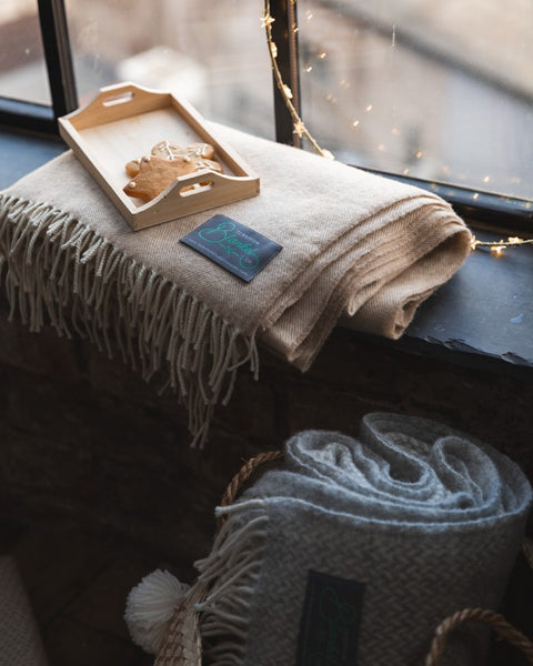 A beige wool blanket folded on a windowsill with a wooden tray of snowflake cookies on top