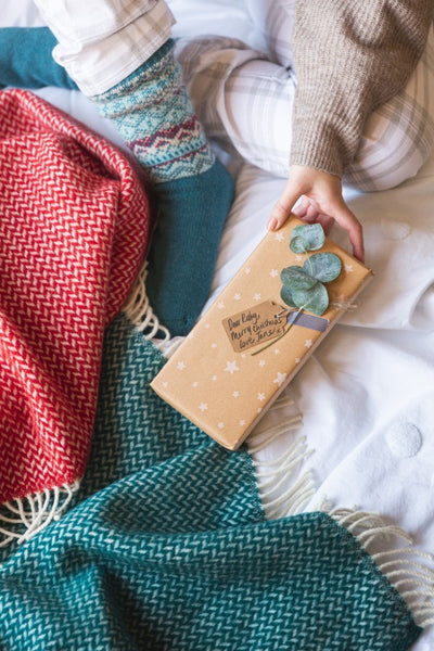 Red and green wool blankets on a bed with person holding Christmas present