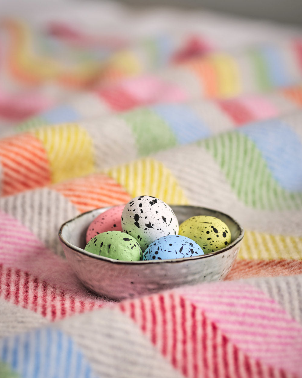 bowl of colourful mini eggs on a rainbow stripe wool blanket from The British Blanket Company