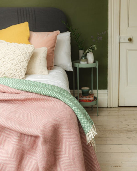 bedroom styled for spring with pink and sage green wool blankets layered on a bed