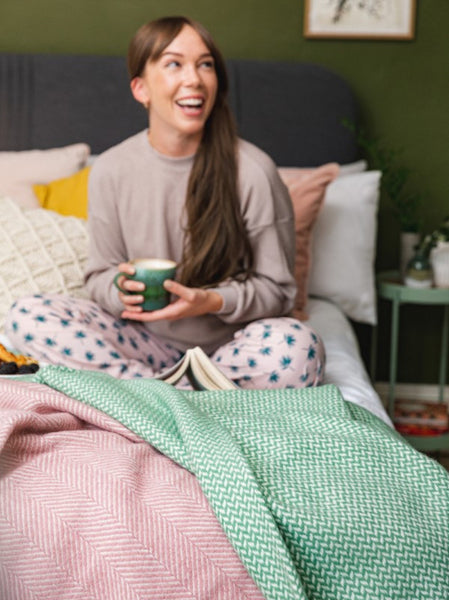 laughing woman in a cosy bedroom styled for spring with pink and green wool blankets layered on the bed