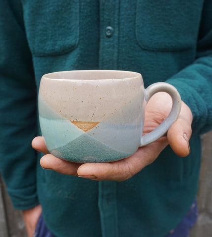Person in blue shirt holding a multicoloured ceramic mug