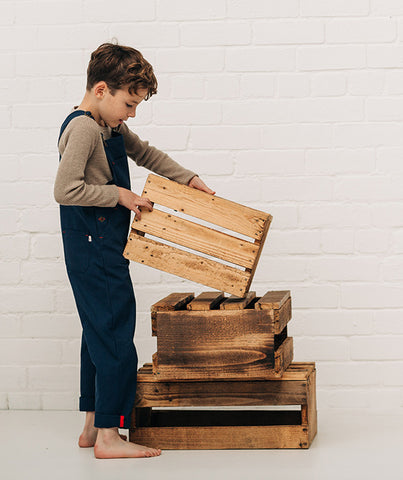 Boy stacking wooden creates wearing navy blue dungarees and beige top