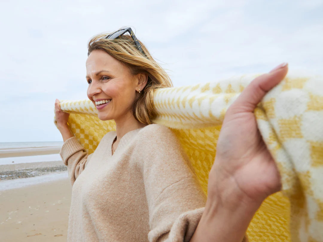 smiling woman on beach with a yellow blanket from The British Blanket co - mothers day gifts for her blog