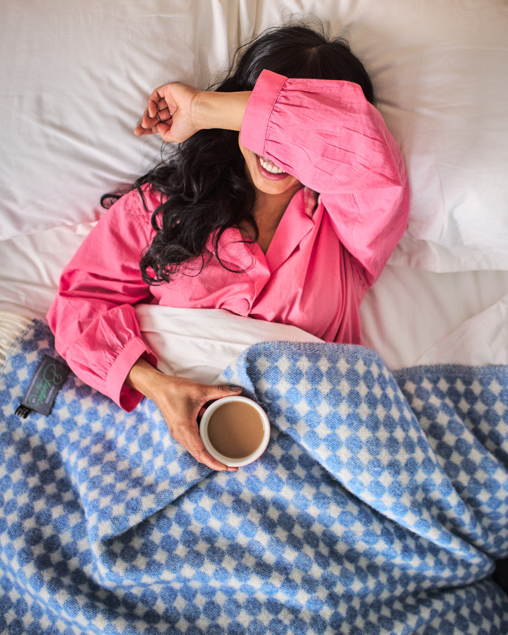 smiling woman in bed covered in a blue spotty wool blanket from The British Blanket Company