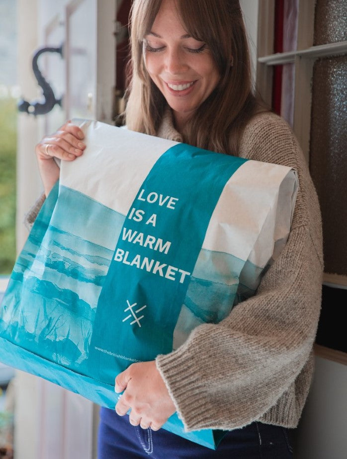 Smiling woman receiving a wrapped parcel containing a blanket from The British Blanket Company