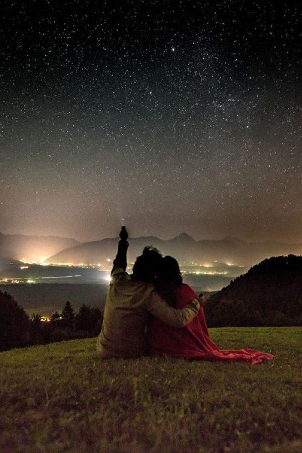 couple wrapped in a blanket stargazing on a hillside