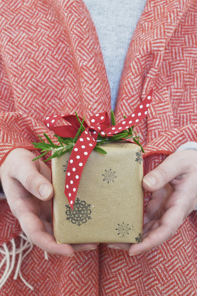 person wrapped in red wool blanket holding gift wrapped in brown paper