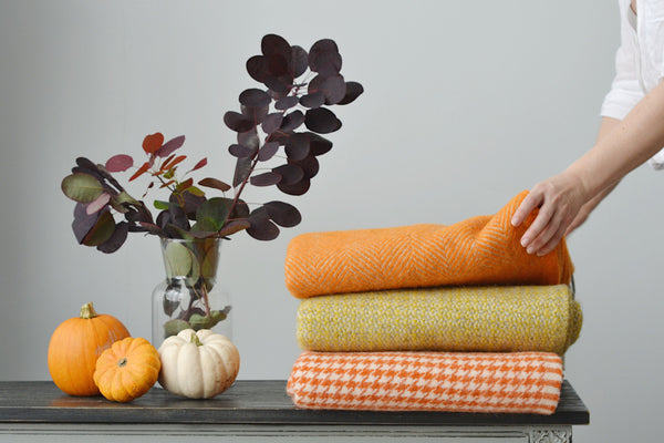 stack of orange and yellow autumn blankets with pumpkins alongside