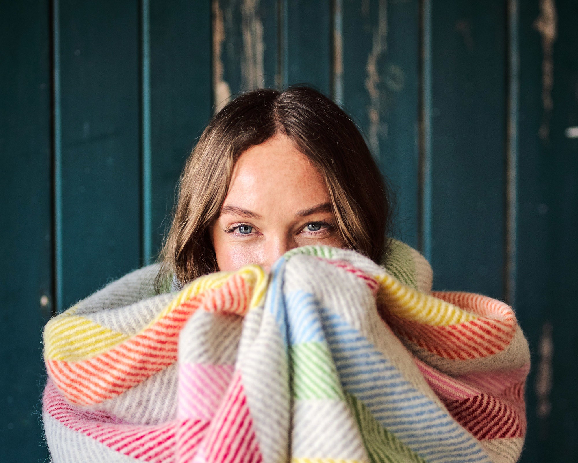 Smiling woman wrapped in rainbow stripe wool blanket from The British Blanket Company