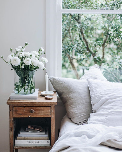 cool summer bedroom with an open window and white linen sheets and a vase of white flowers on the bedside table photograph by Abbie Melle