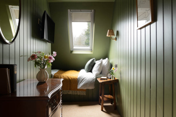 cosy loft bedroom with green painted panelling and a yellow wool blanket
