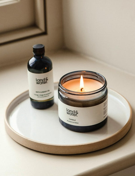 Candle and skincare product on a ceramic tray on a windowsill