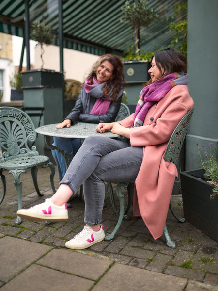 two women sitting outside a cafe wearing oversized blanket scarves from The British Blanket Company