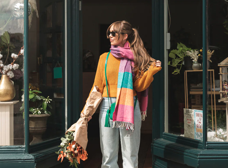 wwoman in the doorway of a florist wearing a colourful  pashminas and blanket scarves The British Blanket Company