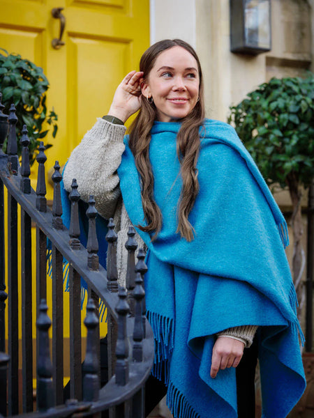 woman in front of a yellow door wearing blue wearable blanket wrap from The British Blanket Company