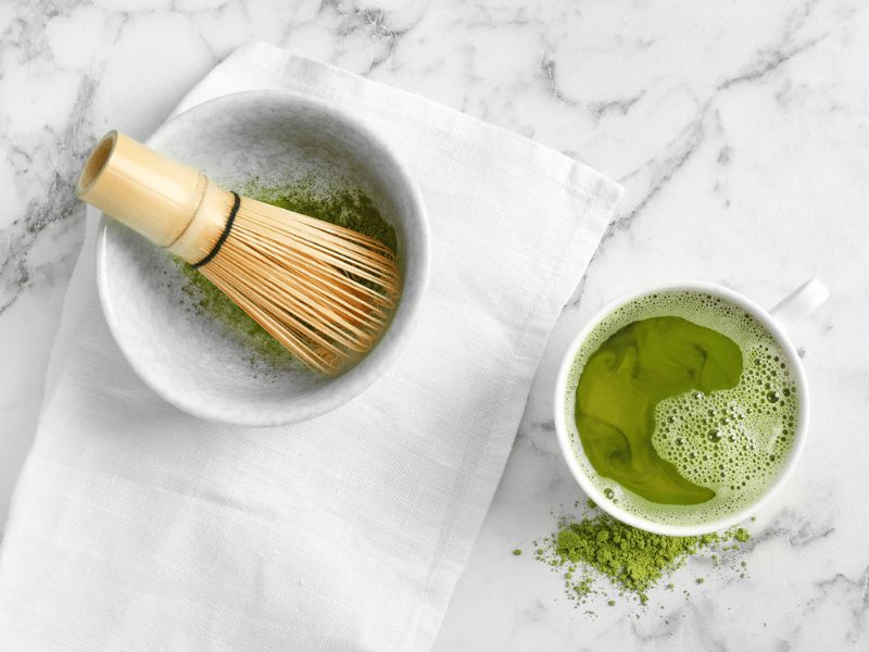 A bowl of matcha tea and bamboo whisk on a granite stone slab