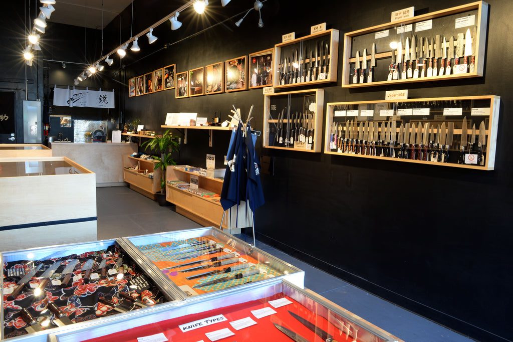 A photo of the Seisuke Knife Portland shop interior showing display cases on the walls and tables containing a large selection of knives