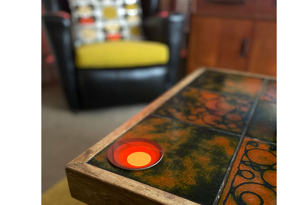 A 70s style coaster sits on a vintage tiled coffee table, in the blurred background is a vintage armchair