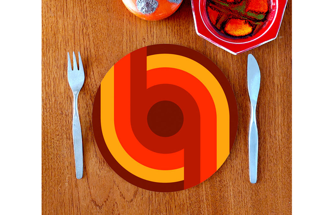 A 70s style placemat featuring retro Supergraphics sits on a teak table with mid century knife & fork and vintage crockery