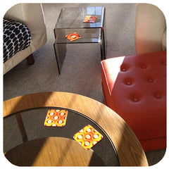 Orange 1970s style op art coasters on vintage glass coffee tables in a retro styled lounge.