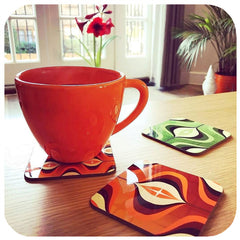 &0s Op Art Coasters in Orange and Green on table with tea cup