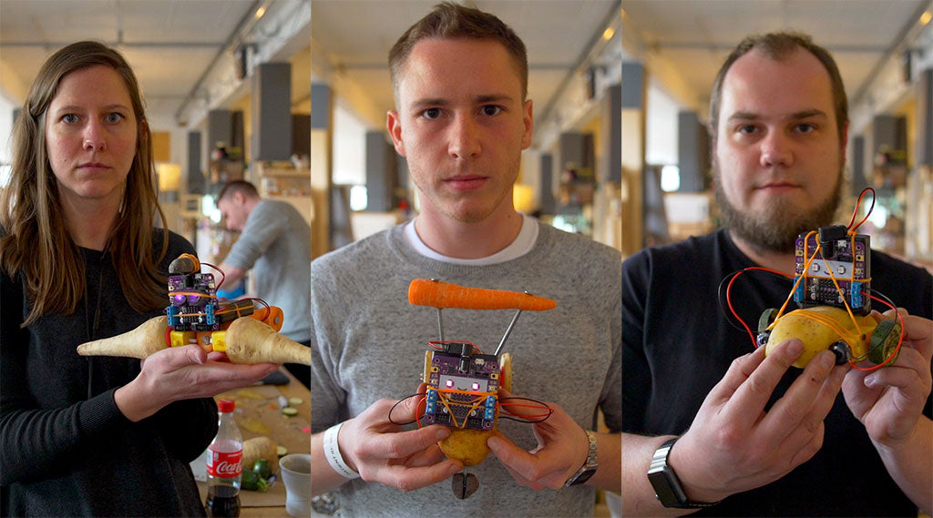 Three young adults holding robots made from vegetables and staring intently into the camera
